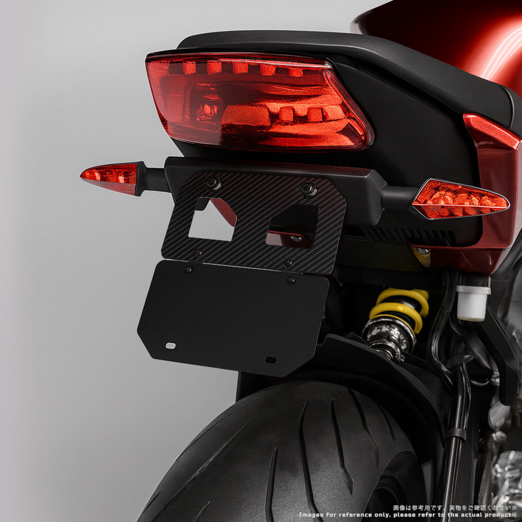 125cc以下対応・山型サイズ｜プレート未装着の VARQON カーボン製ナンバープレートフレーム（ブラケット）リア斜めクローズアップ。軽量カーボン、配線しやすい開口設計、原付二種に最適。